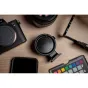 Techart TCS-04 bayonet adapter for Canon EF/Sony E with Quick Back button and tripod mount, placed on a wooden surface alongside a Canon camera body, detached lens, smartphone, and color calibration chart.
