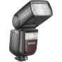 Godox Speedlite V860III zibspuldze uzstādīta uz kameras ar bezvadu trigeri, ar taisnstūra difuzoru un LED indikatoru, uz maroon paneļa redzams 'Godox' logo.