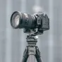 Falcam apļveida pusējo turētājs ar ātri atbrīvošanas mehānismu, piestiprināts pie Sony bezspoguļu kameras ar lielo objektīvu uz statīva, demonstrējot horizontālā un vertikālā režīma maiņas iespēju