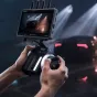 DJI Focus Pro Hand Unit для точной настройки фокуса в профессиональной киносъемке, удерживаемый человеком с монитором, отображающим прямую трансляцию автомобиля, снимаемого при драматическом освещении.