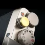 JJC SRB‑NSCDGD soft release button with a golden brass cap mounted on a camera top panel, featuring a textured grip and surrounding mode dial, a spare parts accessory for Fujifilm, Sony, Panasonic, Leica, and Canon cameras.