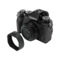 JJC LH JXF23M2 melna lēcas aizmugura Fujifilm XF 23mm/27mm objektīviem ar magnētisko fiksāciju, novietota blakus Fujifilm bezspoguļu kamerai.