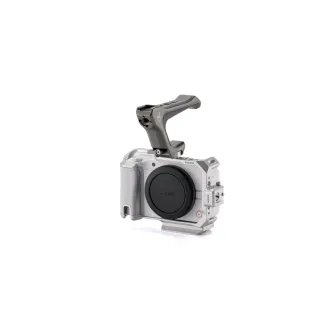Крепление-кедж Tilta для Canon R50 V серебристого цвета с съемной ручкой NATO и ARCA-платформой, вид спереди с интегрированной эргономичной рукояткой и отсеком для объектива