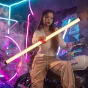 Световая палочка Viltrox K90 Dual RGB излучает яркий желтый свет, удерживаемая горизонтально человеком в повседневной одежде, окруженная неоновыми огнями и дымовыми эффектами, подчеркивая ее элегантный дизайн и портативность.