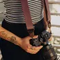 Peak Design Slide Lite camera strap with Anchor Link system attached to a mirrorless camera, showcasing sleek brown webbing and dual quick-adjusters for versatile wear styles.