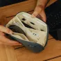 Peak Design Tech Pouch Small okeāna zilā kompaktā organizatora ar 12 elastīgām kabatiņām, atvērtā skatījumā redzami iekšējie nodalījumi kabeļiem, USB zibatmiņām un aksesuāriem uz koka galda