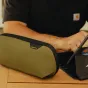Компактный органайзер Peak Design Tech Pouch Small в цвете kelp с эластичными петлями для ручек и аксессуаров, частично открытый на деревянном столе.
