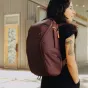 Burgundijas Peak Design Everyday Backpack Zip V2 15L, modernas, lauksargā un fotoaparatam paredzēta soma ar 270° pieeju un pielāgojamu iekšējo organizāciju, ko valkā persona telpās blakus kāpnēm.