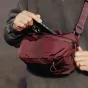 Peak Design Outdoor Sling 4L maroon krāsā ar laika apstākļiem izturīgu Terra Shell audumu, demonstrējot regulējamu remenu sistēmu un magnētisko aizdari priekšējā kabatā.