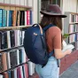 Рюкзак Peak Design Everyday Backpack Zip V2 15L темно-синего цвета из водостойкого переработанного нейлона 400D, носимый человеком в городской обстановке возле книжных полок