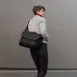 Peak Design Everyday Messenger V2 13L black crossbody bag with padded shoulder strap in use by a person against a plain gray wall