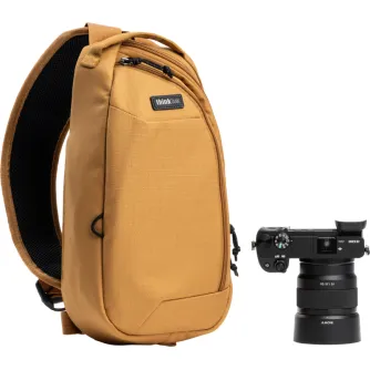 Think Tank TurnStyle 5L Golden Hour siksnas soma ar melnu sietu aizmugures paneli, divām rāvējslēdzēju kabatām, drošu priekšējo kabatu un kameru klipšu sliedi, blakus ir Sony Alpha DSLR ar 24-70mm objektīvu.