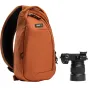 Слинг-сумка Think Tank TurnStyle 5L Urban Rust с черной сетчатой задней панелью, с основным отделением на молнии, карманом для планшета и карманом для бутылки с водой, рядом с черной камерой с объективом Sony.