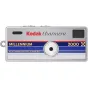 Kodak Charmera Millennium – sudraba krāsas atslēgu piekariņa digitālā kamera ar apaļu objektīvu, zilu un sarkanu svītru dizainu, tekstu 'MILLENNIUM' un '2000', kā arī mazu melnu skatu meklētāju.