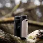 GPO PASSION 8x32ED binoculars with black and beige housing, featuring an adjustment dial and eyepiece on the left and an objective lens with strap attachment on the right, resting on a moss-covered tree branch with blurred fores