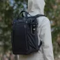 PGYTECH OneGo Roamer Tote Backpack 18L matēta melna kameras soma ar sānu kabatu, kurā ir statīvs, uz auduma redzamas ūdens pilieni, to nēsā cilvēks baltā lietusmētelī ārā