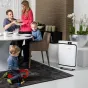 BONECO P500 air purifier on the floor beside a modern dining area where a family enjoys a meal and a child plays, showcasing its sleek white design in a home setting.