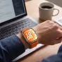 Tech-Protect oranžs neilona rokas siksna Huawei Watch Fit sērijai, elpojoša un ātri pievienojama, valkāta uz rokas pie galda ar datoru un kafijas krūzi.