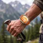 Tech-Protect oranžs neilona pulksteņa siksna Huawei Watch Fit sērijai, elpojoša un regulējama, uz sviedriem klāta roka, turot pārgājiena nūju kalnu fona.