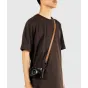 Peak Design Form Leather tan kameru siksna, kas nēsā pār cilvēka krūtīm, ar zemu profilu Anchor Link savienotājiem un pievienotu melnu kameru, minimālistisks pilnīgas ādas dizains