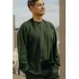 Peak Design черный ремень для камеры из полноразмерной кожи с низкопрофильными быстрыми соединителями, длиной 134 см, надетый на мужчину в зеленом свитере, камера висит сбоку на фоне размытого городского пейзажа.