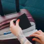 Tuvplāns ar tetovētām rokām ar spilgti sarkanu nagu laku, kas ievieto melnu Peak Design pasē vālietu atvērtā bordo koferī, kurā redzama National Airlines First Class karte kabatā un vālieta 'pd' logo uz virsmas.