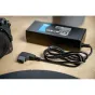 Newell D‑Tap 16.8 V 5 A V-mount battery charger with coiled cable and D‑Tap connector, placed next to a Nikon camera on a wooden surface