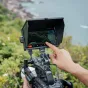 Viltrox DC A1 7‑pēdu supergaismas HD skārienekrāns ar noņemamu saules aizsargu, uzstādīts uz Sony kameras, roka regulē iestatījumus, filmējot piekrastes ainavu ar zaļām lapām